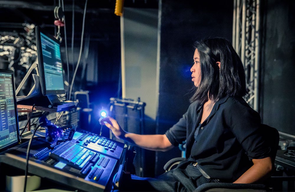 A woman works at a lighting desk in a theatre.