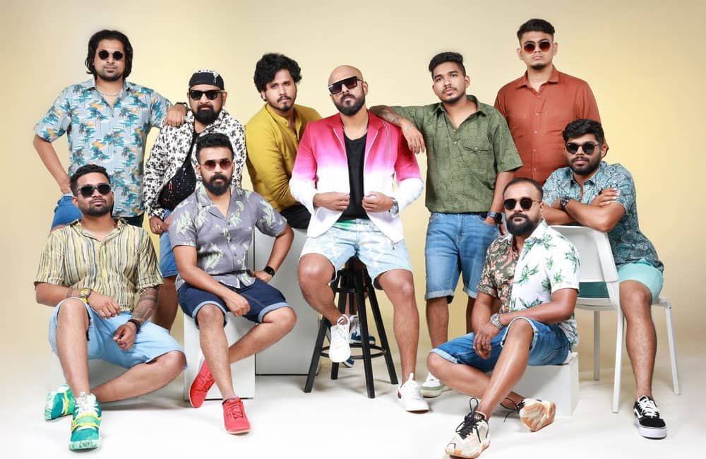 Photo features a group of 10 Indian men, wearing brightly coloured casual clothes.
