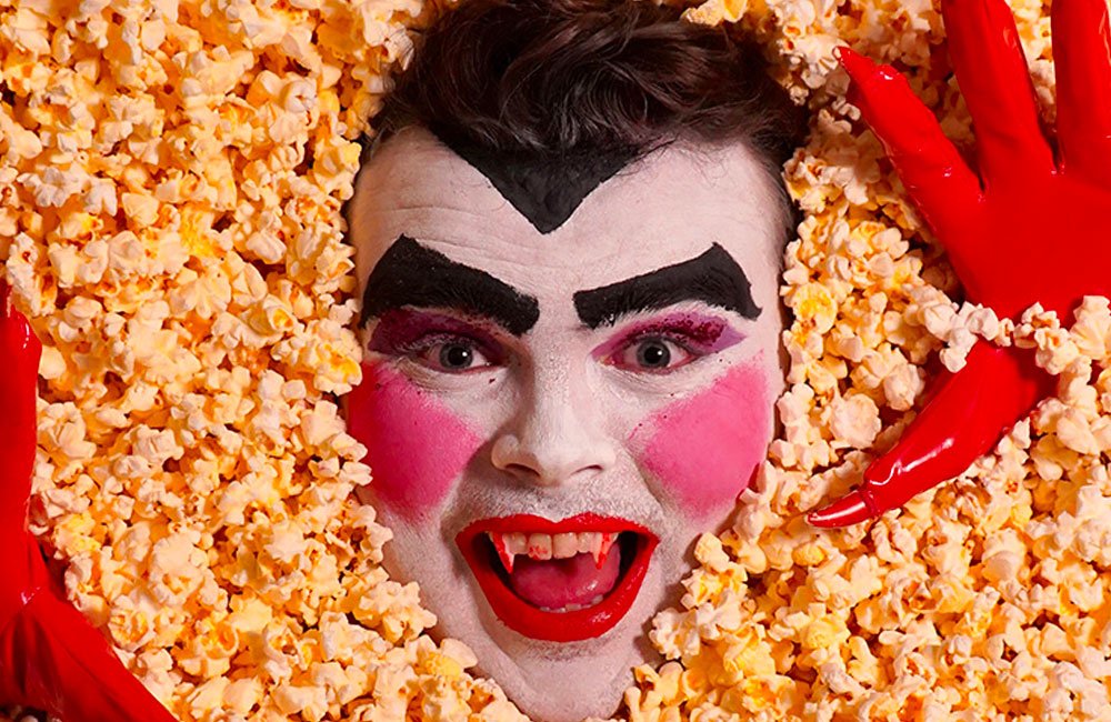 A man's face wth over the top Dracula make up emerges from popcorn.