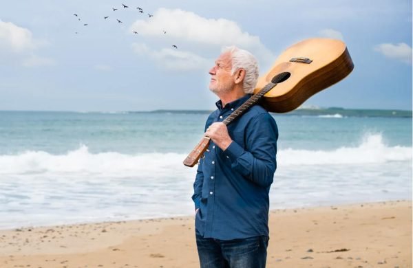 A man stands on a beach holding a guitar.