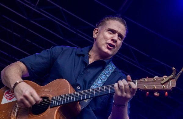 Photo of a male performer holding a guitar on a stage.