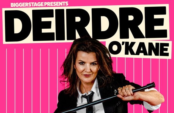 Comedian Deirdre O'Kane. She is wearing a business suit and holding a whip.