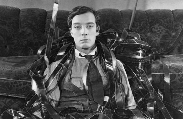 A black and white image of silent movie star Buster Keaton surrounded by unspooled rolls of film.