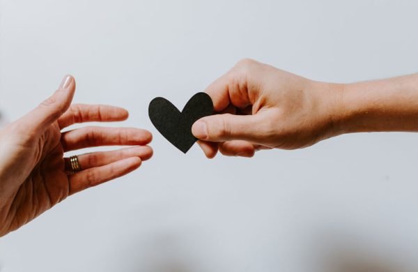Image shows a hand holding a paper heart out to another hand.